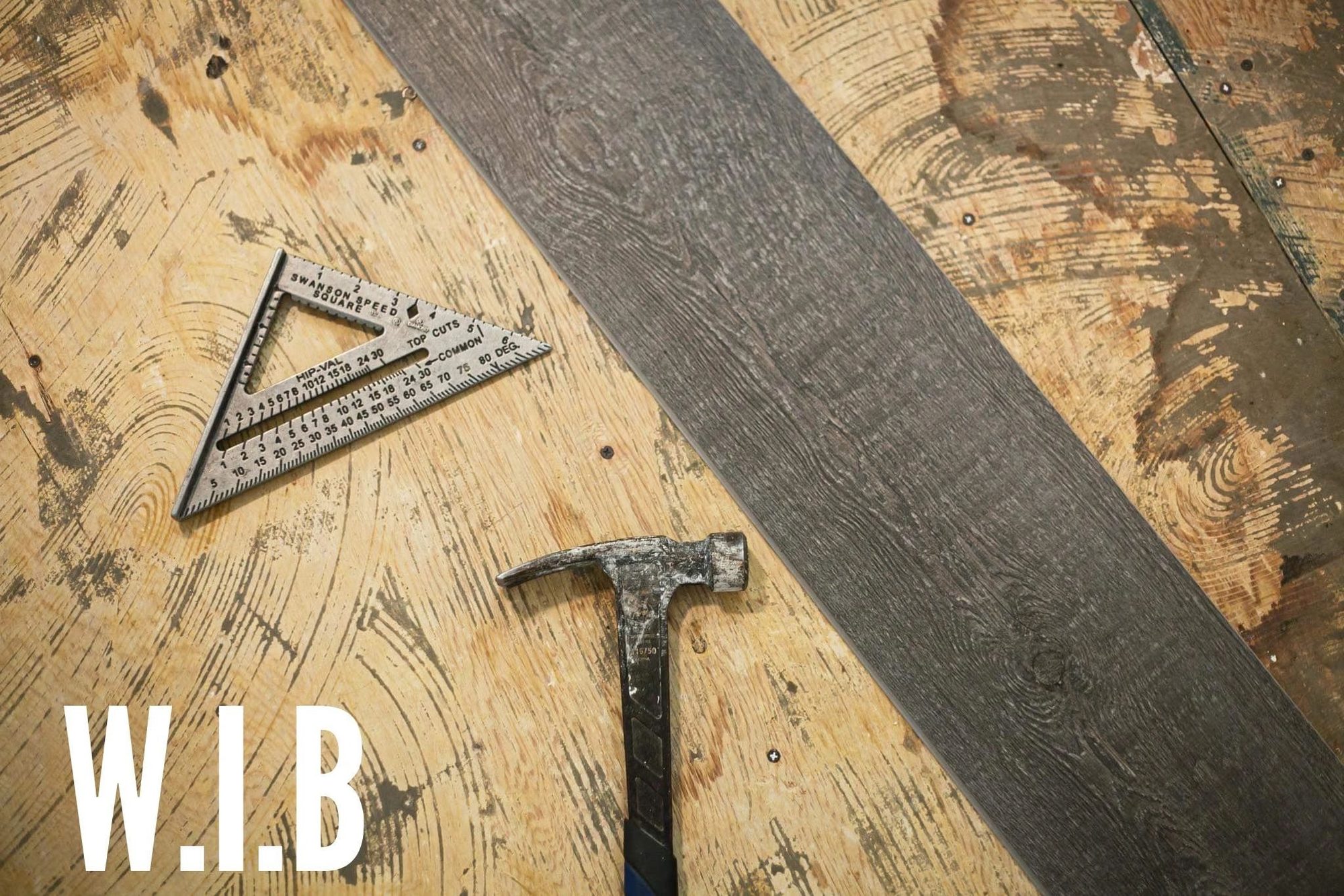 A speed square and hammer resting on a fresh timber beam, marked W.I.B — Western Idaho Builders' own tools of the trade